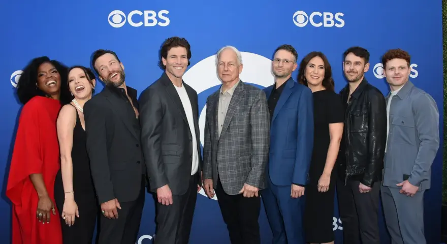 Die Besetzung von Navy CIS: Origins posiert auf einem blauen Teppich vor dem CBS-Logo.