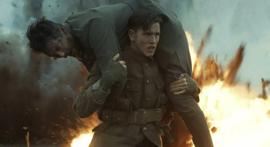 Harris Dickinson trägt einen verwundeten Kameraden durch Explosionen. Ein dramatischer Moment aus seinen Filmen.