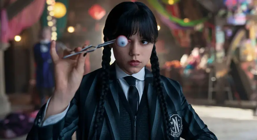 Wednesday Addams hält mit einer Pinzette ein künstliches Auge vor ihrem Gesicht. Ein Blick auf die kommende Staffel 2 von Wednesday.