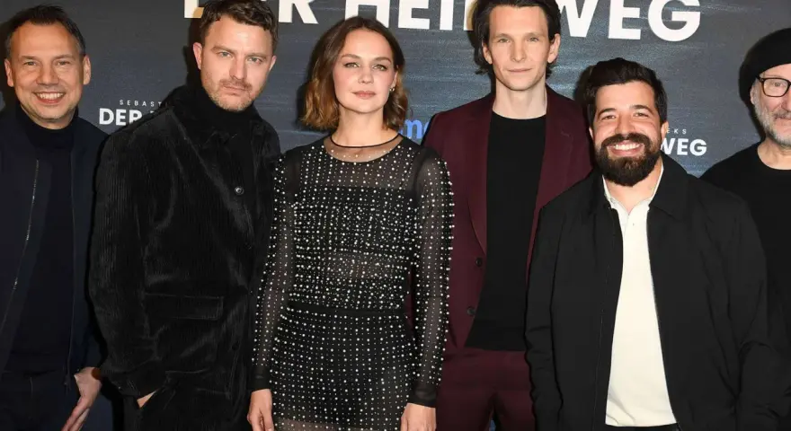 Das Ensemble des Films "Der heimweg" posiert lächelnd vor dem Banner.