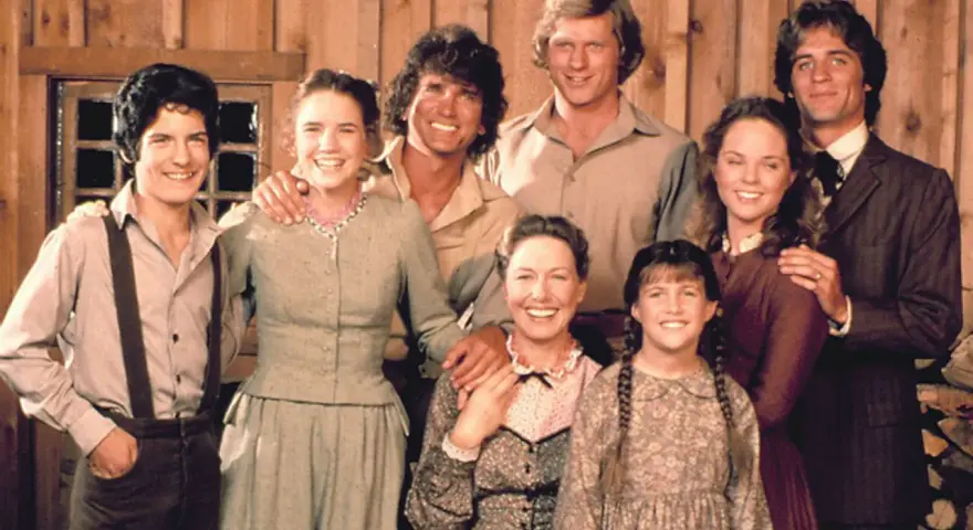 Die Besetzung von Unsere kleine Farm: Eine glückliche Familie posiert vor einer Holzwand.