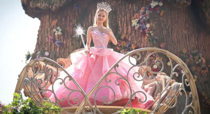 Ariana Grande als Glinda im Film "Wicked", in einem rosa Ballkleid und mit Zauberstab.