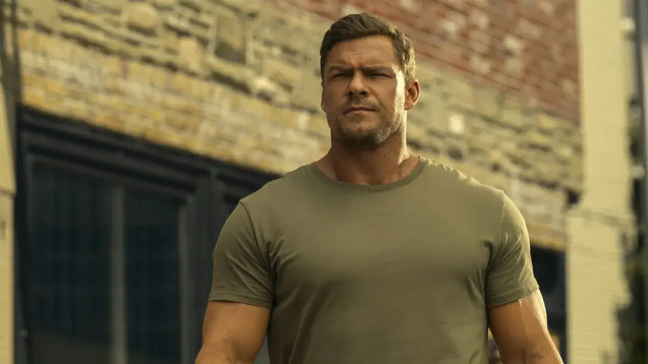 Ein muskulöser Mann mit kurzem Haar und Bart, trägt ein olivgrünes T-Shirt. Er blickt nachdenklich in die Ferne. Möglicherweise ein neuer Fall für Reacher Staffel 4.