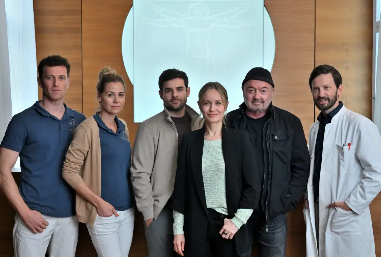 Sechs Personen stehen vor einer Holzwand. Ein starkes Team, das bereit ist, Herausforderungen anzunehmen.