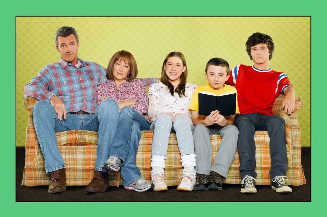 Die besetzung von The Middle sitzt auf einer Couch: Vater, Mutter, Tochter, Sohn und ein weiterer Sohn, der ein Buch hält.