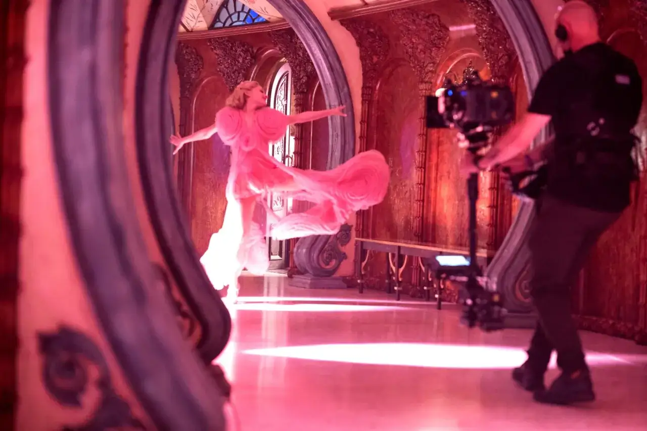 Dreharbeiten für Ariana Grandes neue Filme. Eine Tänzerin in einem rosa Kleid wirbelt, während ein Kameramann filmt.