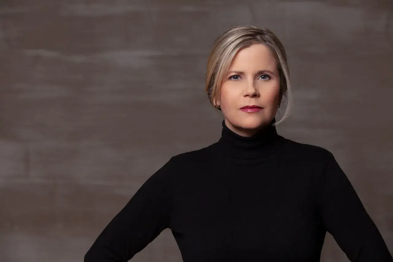 Porträt einer Frau mit blonden Haaren und einem schwarzen Rollkragenpullover. Sie könnte eine Schauspielerin sein, die in Filme von Michaela Schaffrath mitspielt.