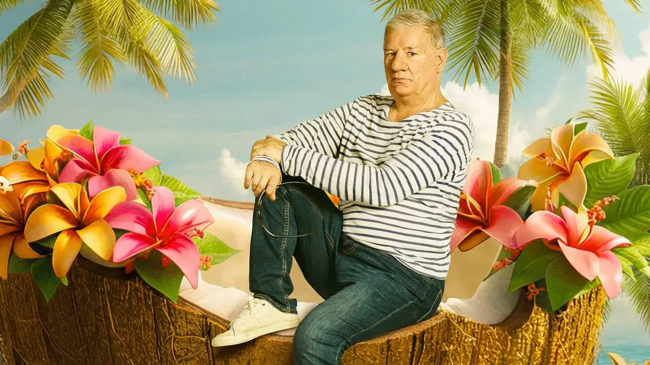 Mann in gestreiftem Shirt sitzt in einer Kokosnussschale, umgeben von tropischen Blumen und Palmen. Ein Bild, das an Filme von Claude-Oliver Rudolph erinnert.