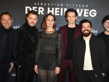 Das Ensemble des Films "Der heimweg" posiert lächelnd vor dem Banner.