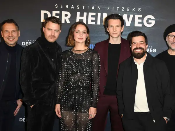 Das Ensemble des Films "Der heimweg" posiert lächelnd vor dem Banner.