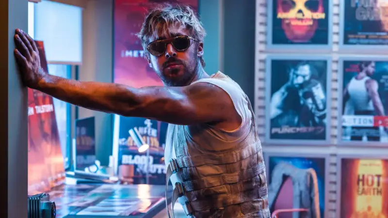 Ryan Gosling in Sonnenbrille, lehnt an einer Wand mit Postern seiner Filme.