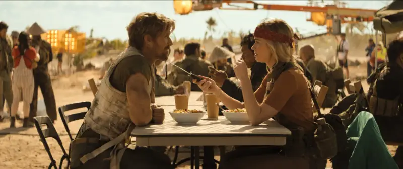 Ein Mann und eine Frau sitzen an einem Tisch, essen und unterhalten sich. Sie könnten die Hauptfiguren in "the fall guy" sein, die sich auf eine gefährliche Mission vorbereiten.